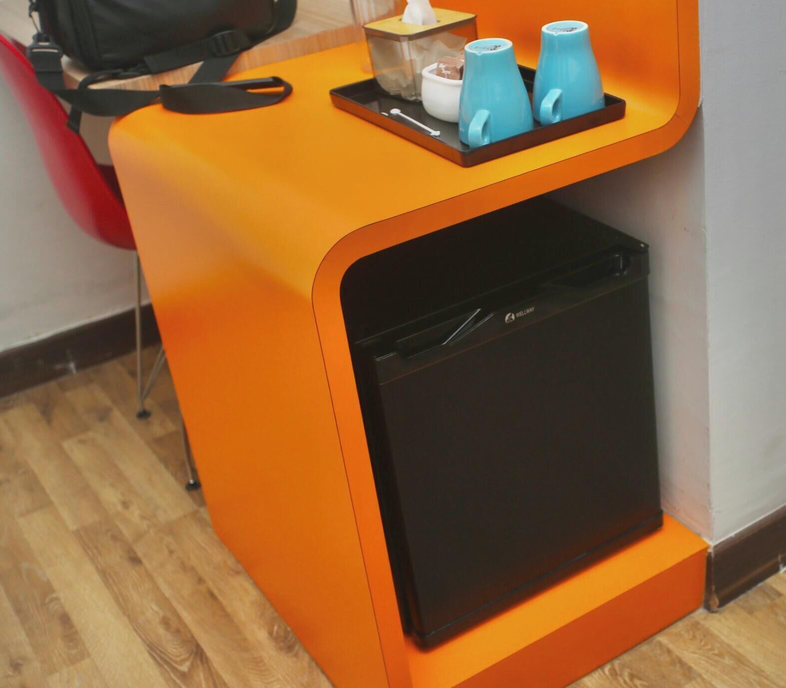 Habitación compacta con un electrodoméstico negro pequeño, posiblemente un refrigerador, y una bandeja con dos tazas azules y una caja de pañuelos.