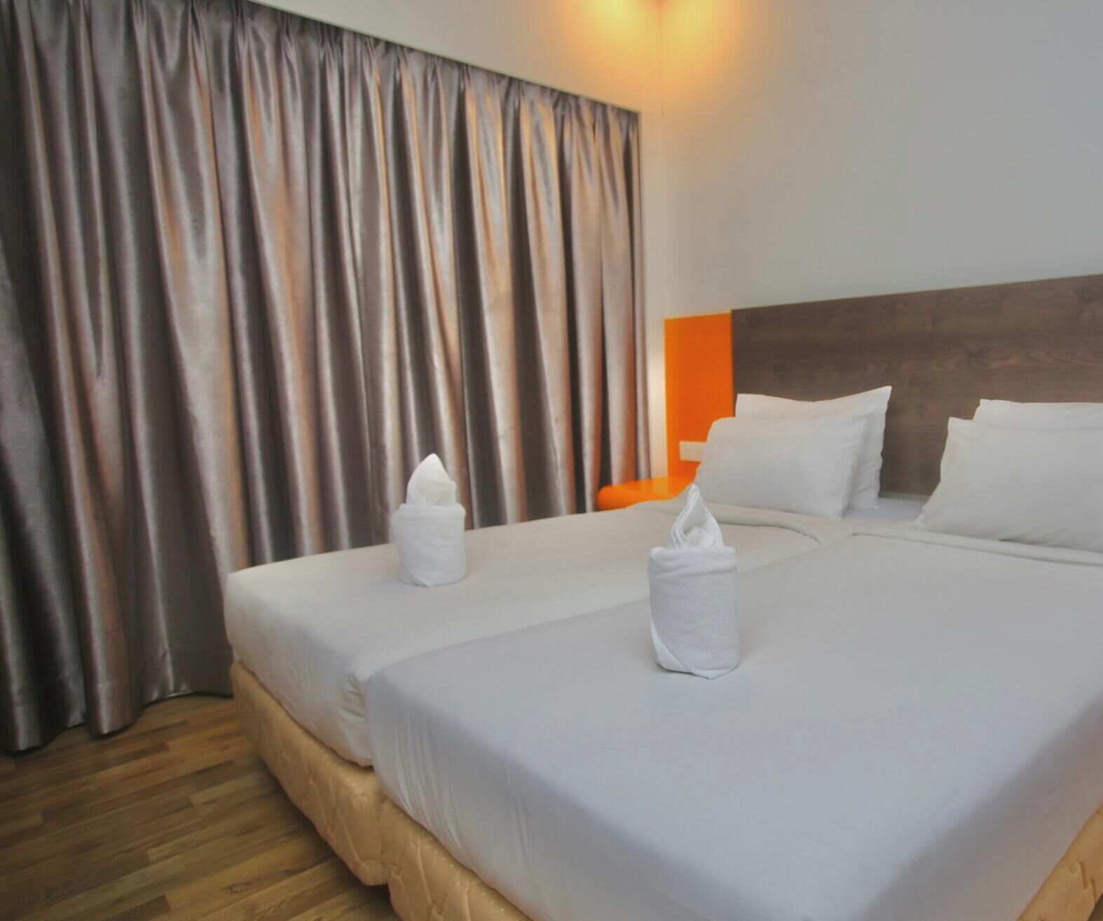 Habitación de hotel con dos camas, piso de madera y una cortina.