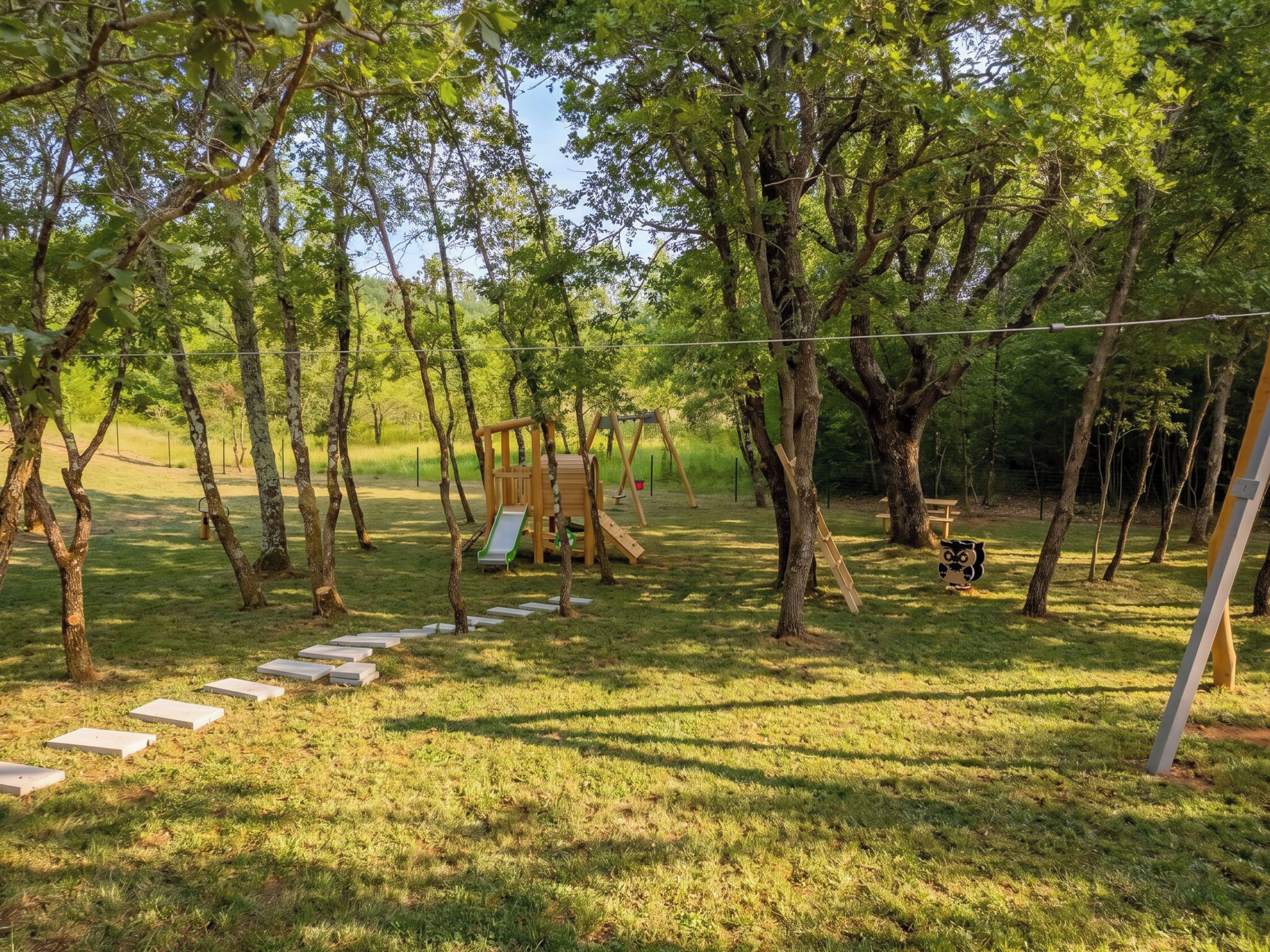 A playground with a slide and climbing structures surrounded by trees.