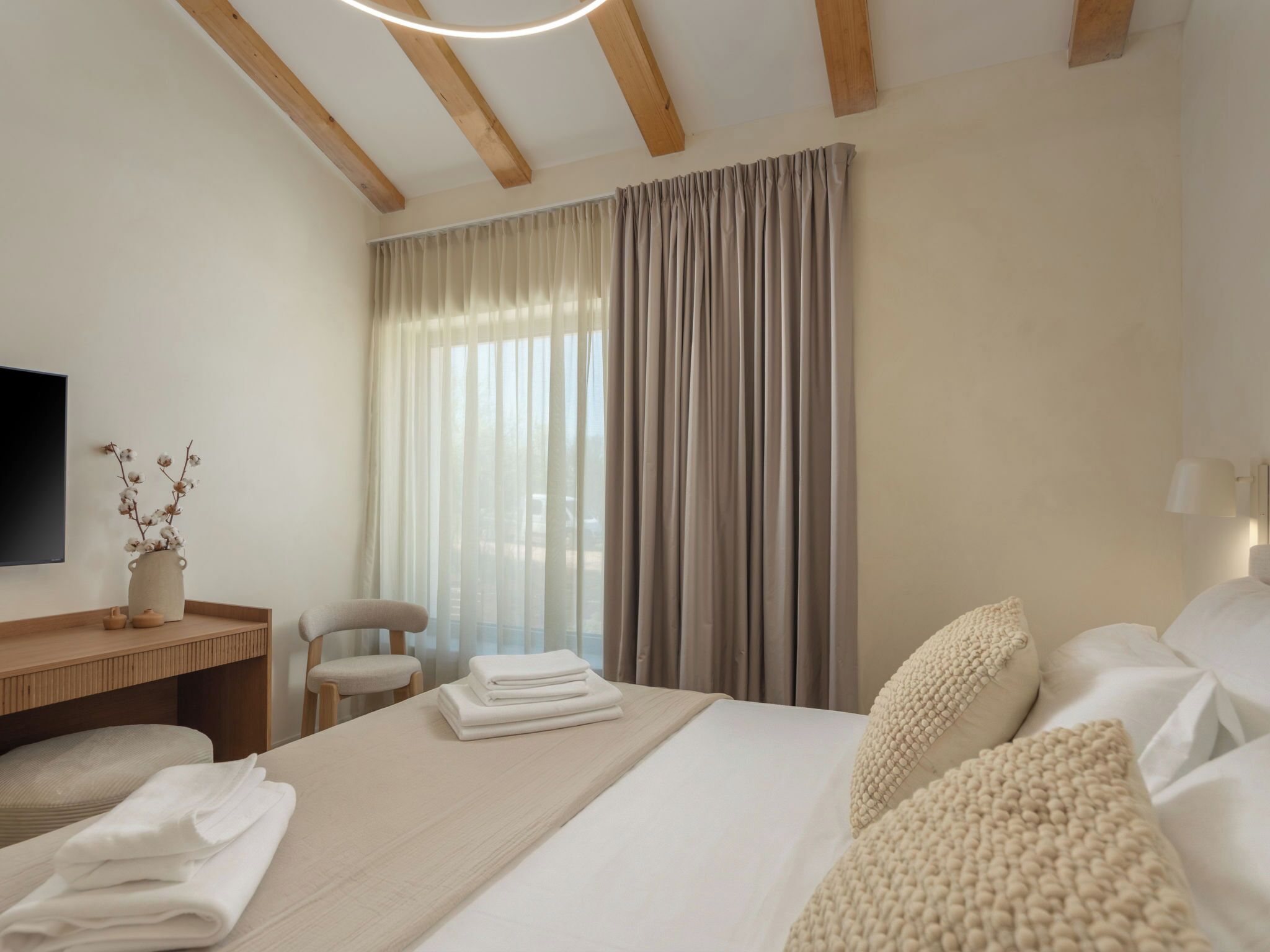 A hotel room with a bed, a desk, a chair, a TV, and a window with curtains.