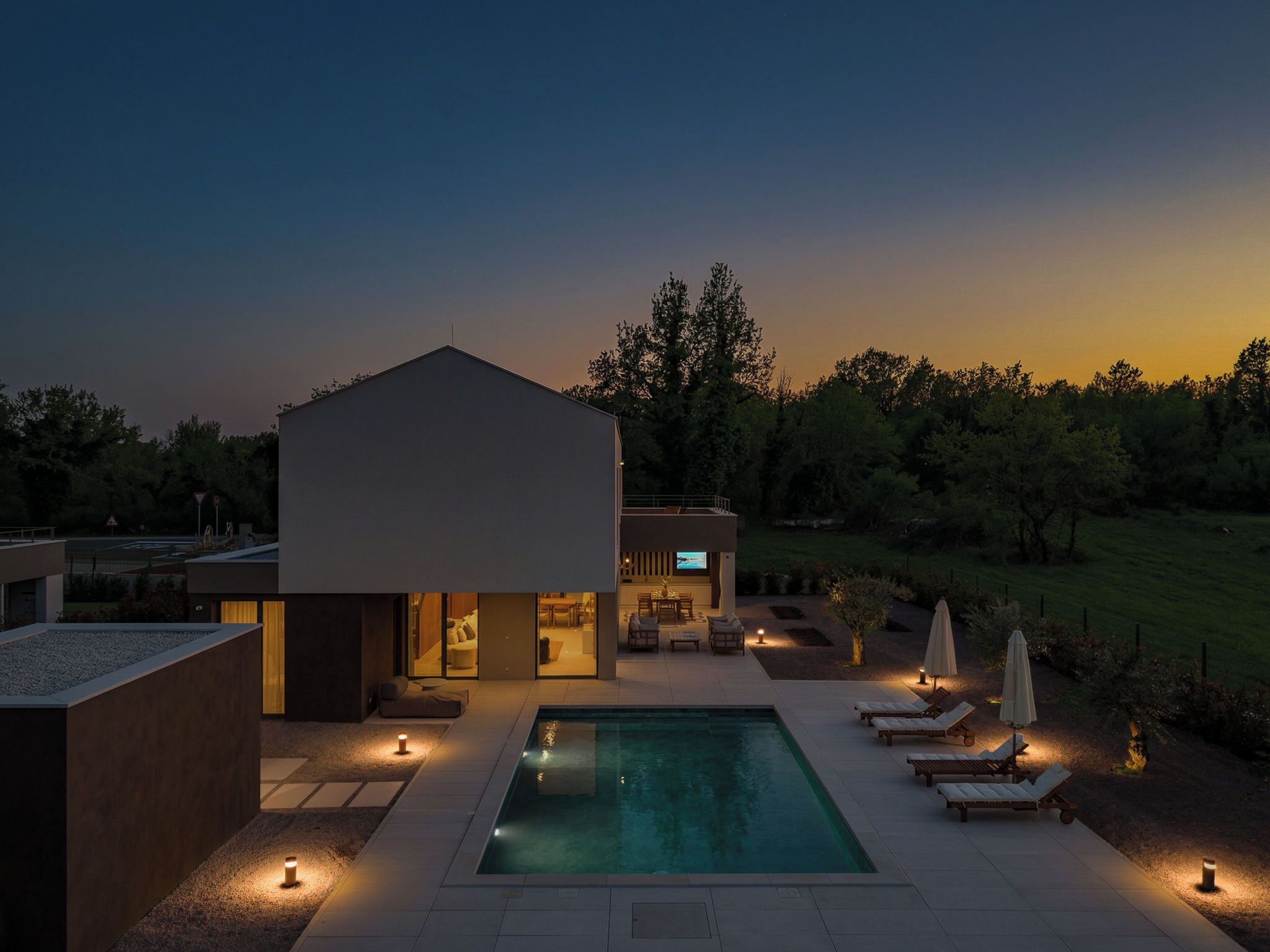 A modern house with a swimming pool, outdoor seating, and a TV in the living area.