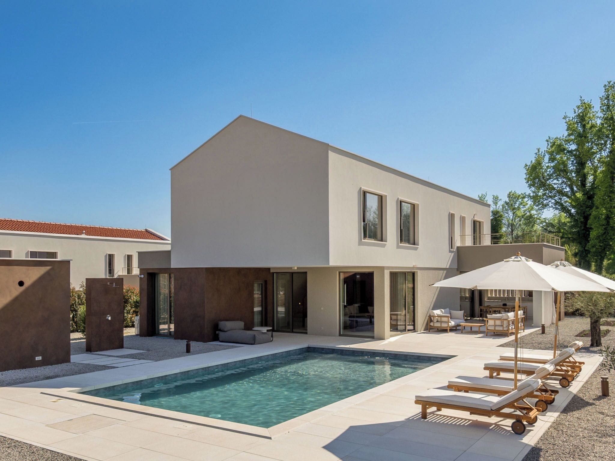 A modern two-story house with a swimming pool, outdoor seating, and a covered patio area.