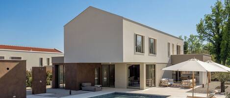 A modern two-story house with a swimming pool, outdoor seating, and a covered patio area.
