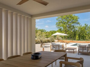 Ein moderner Essbereich im Freien mit Pool, Holzmöbeln und Blick auf die umliegende Landschaft.