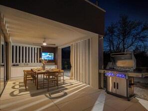 En uteplats med ett matbord, stolar, en grill och en tv-skärm.