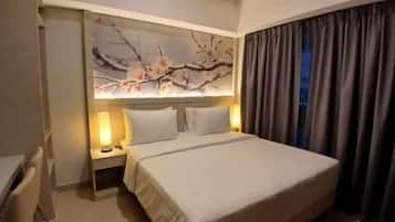 A hotel room with a bed, nightstands, a desk, and a large window with curtains.