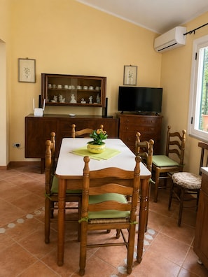 A dining area with a table, chairs, a television, and a cabinet with decorative items. - Villa Brezza Marina (Palmi)