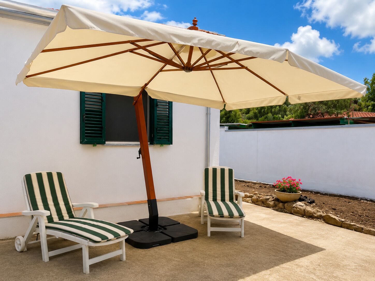 Un patio con due sedie a righe, un ombrellone beige e un piccolo vaso di fiori.