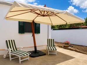 A patio with two striped chairs, a beige umbrella, and a small flower pot. - Villa Brezza Marina (Palmi)