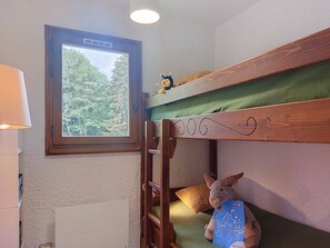 Ein Stockbett mit einer Leiter, ein Fenster mit Blick auf Bäume und ein Stofftier.