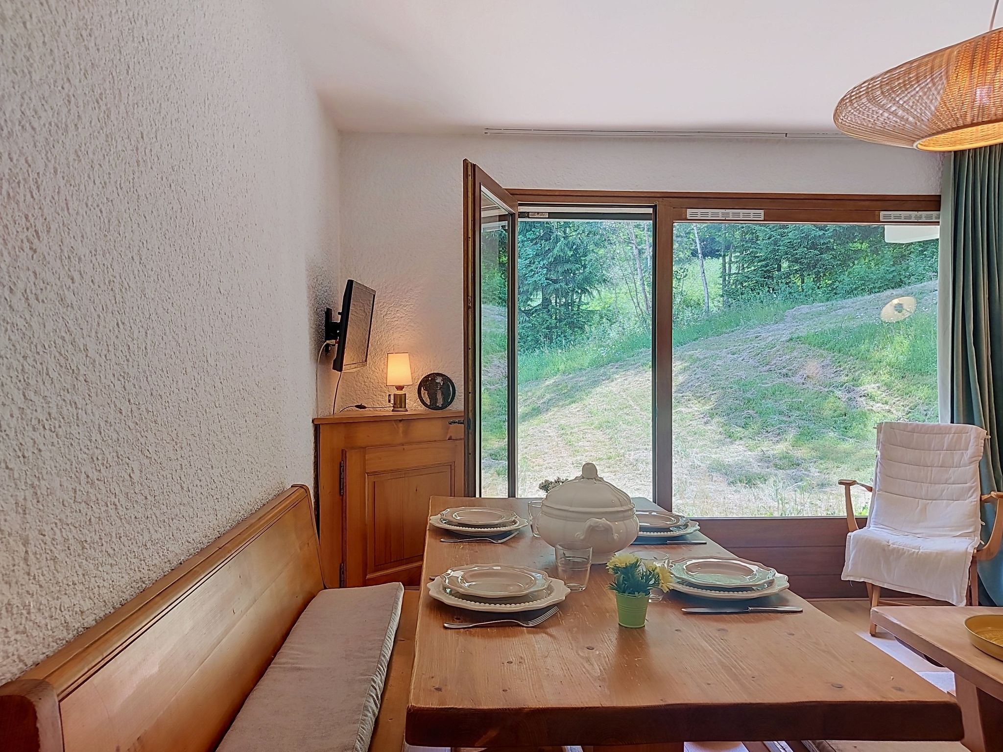 Ein Essbereich mit Holztisch, gedeckt für vier Personen, einer Bank und Blick auf eine grüne Landschaft durch große Fenster.