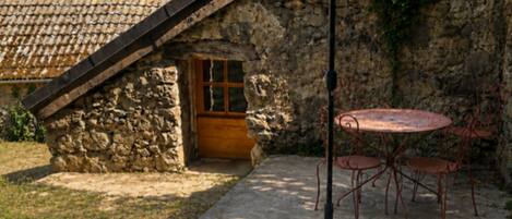 Un edificio de piedra con techo inclinado, un patio con mesa y sillas, y una sombrilla grande.