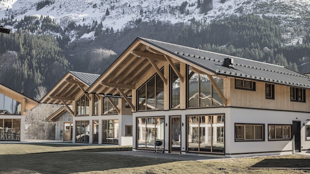 Ein modernes Gebäude mit großen Fenstern und einem geneigten Dach, umgeben von schneebedeckten Bergen.