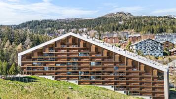 Un hôtel moderne à plusieurs étages, doté d’un toit en pente, de grandes fenêtres et offrant une vue sur un paysage montagneux.