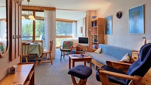 A cozy living room with a sofa, chairs, a table, a TV, and a bookshelf. - Mischabels 20 by Interhome (Crans-Montana)
