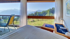 A room with a bed, a chair, a table, and a view of mountains through large windows. - Mischabels 20 by Interhome (Crans-Montana)