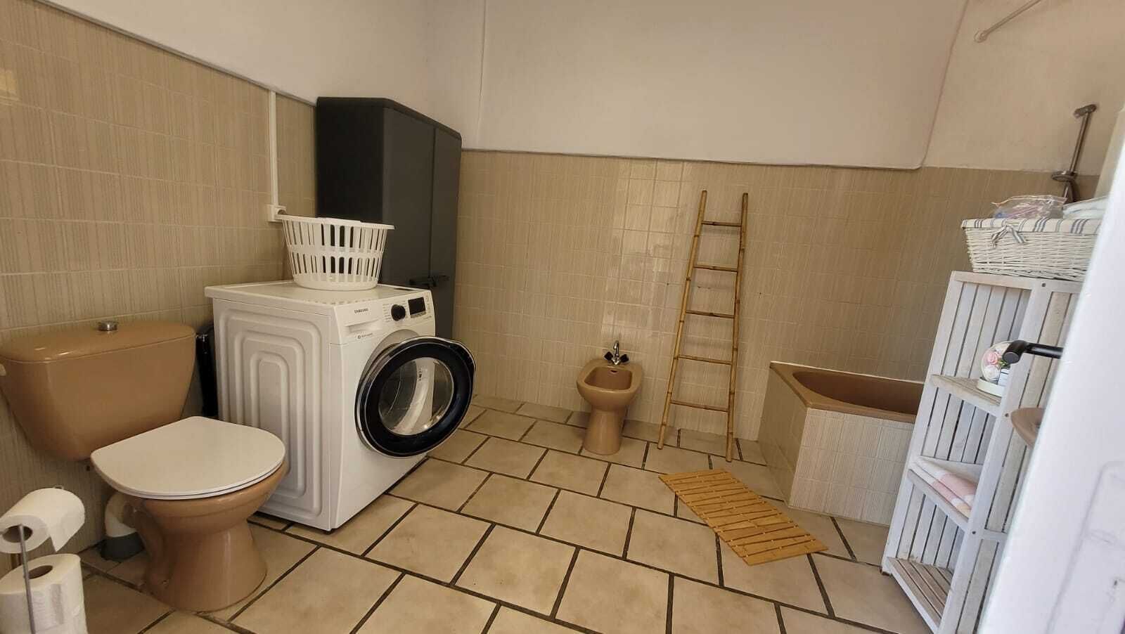 Et lille badeværelse med toilet, vaskemaskine, bidet og badekar.
