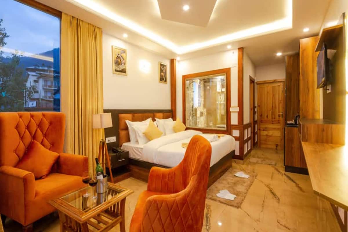 Habitación de hotel con cama, sofá, mesa, televisor y ventana con cortinas.