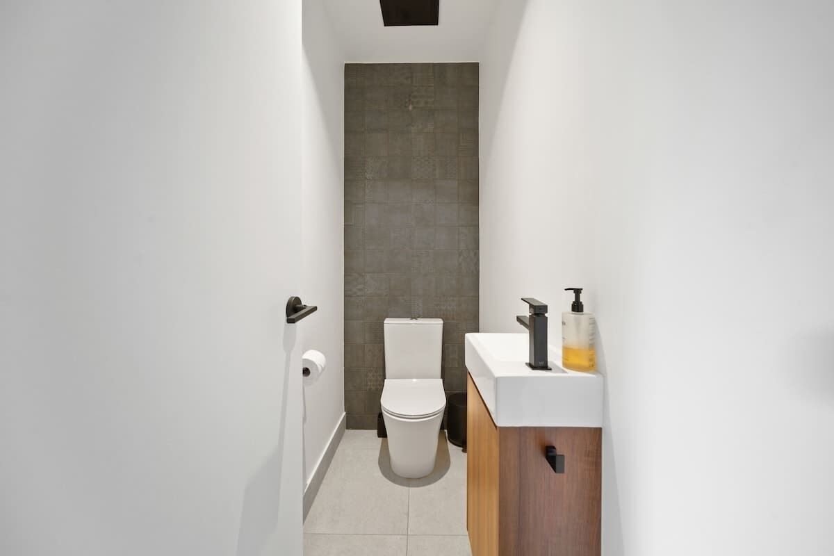 A narrow bathroom with a toilet, a sink with a soap dispenser, and a roll of toilet paper on the wall.