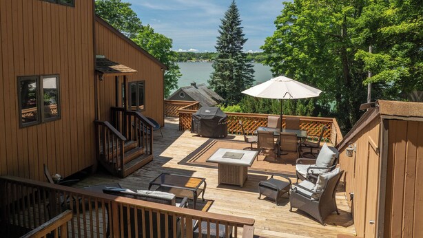 A wooden deck with outdoor furniture, a grill, and a view of a lake. - Em's Lake House - Newly Renovated 5 Bedroom Lake House (Sterling)