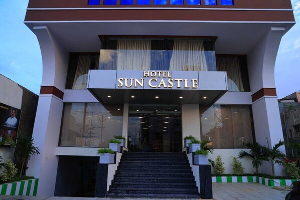 A hotel entrance with a sign reading 'HOTEL SUN CASTLE,' a staircase leading up, and potted plants at the base.