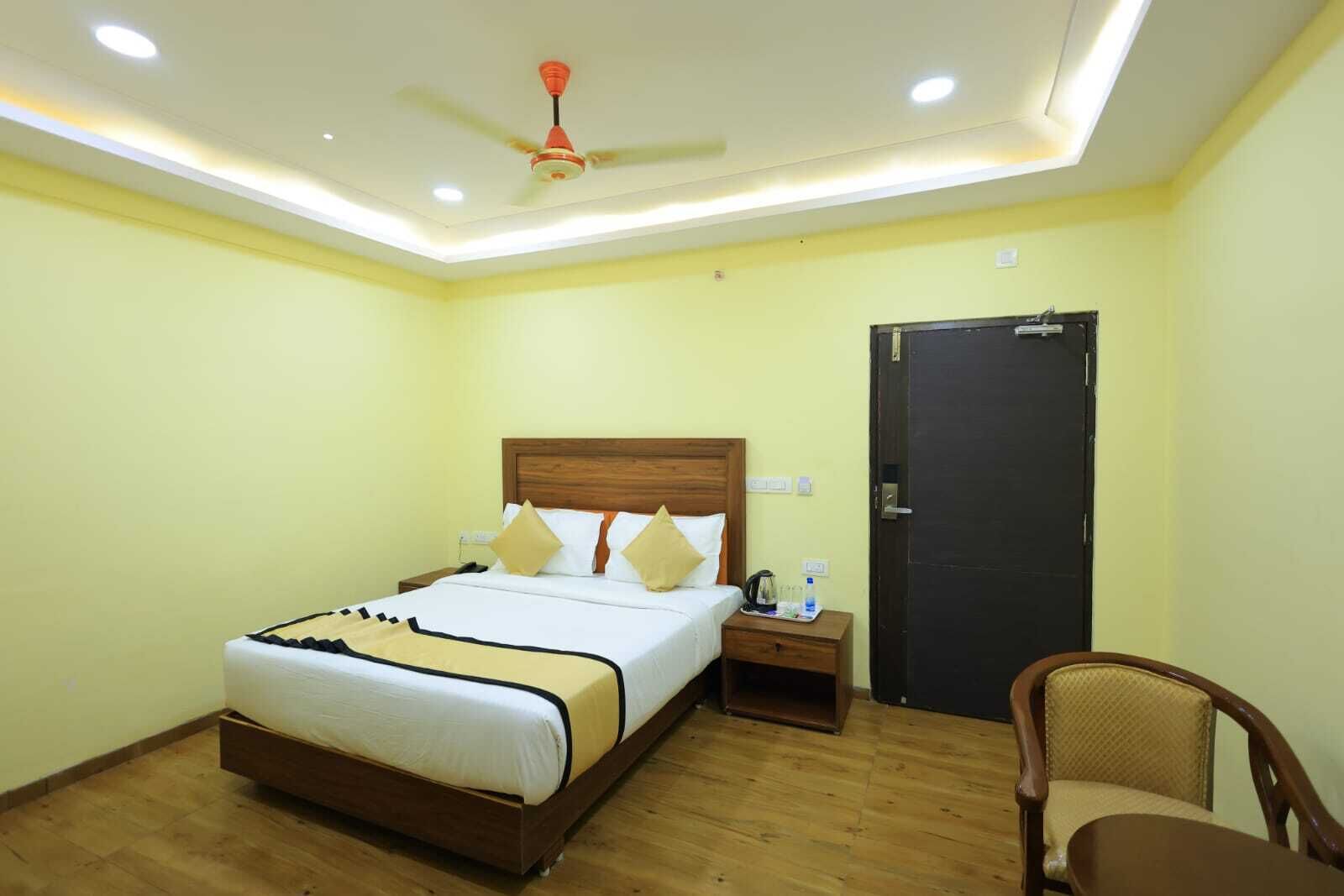 A hotel room with a bed, bedside table, chair, and a door.