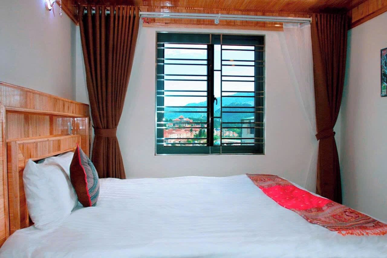 Habitación de hotel con cama, cortinas, ventana con vistas y cabecero de madera.