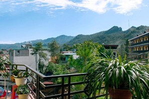 Un balcó amb plantes en testos, vista a un paisatge muntanyós i edificis residencials.