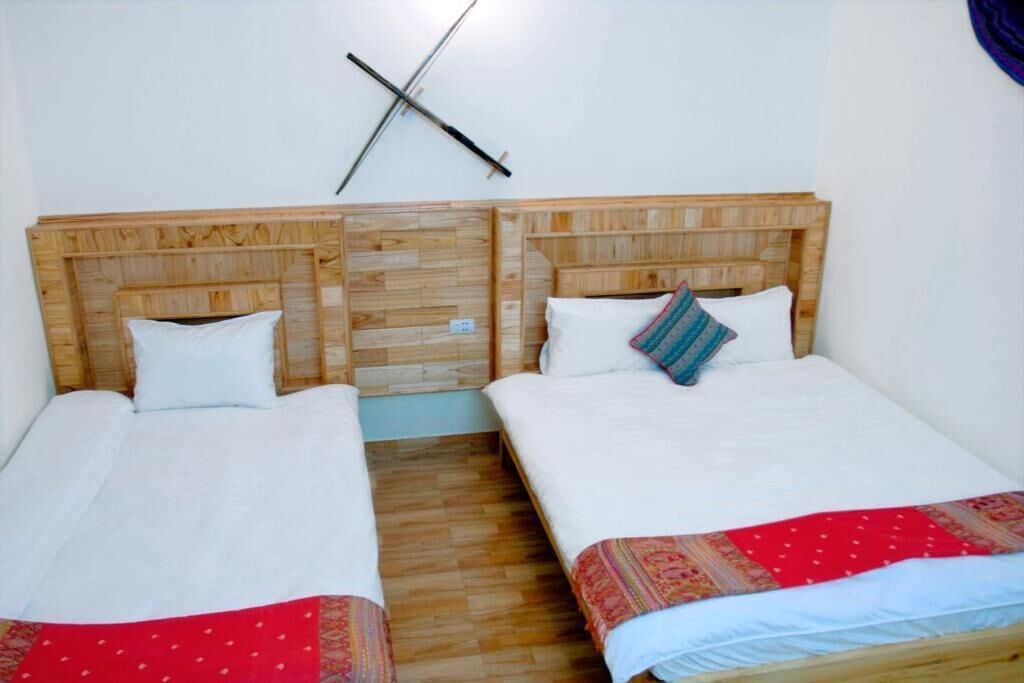 A room with two beds, wooden headboards, white bedding, and a wall-mounted cross.