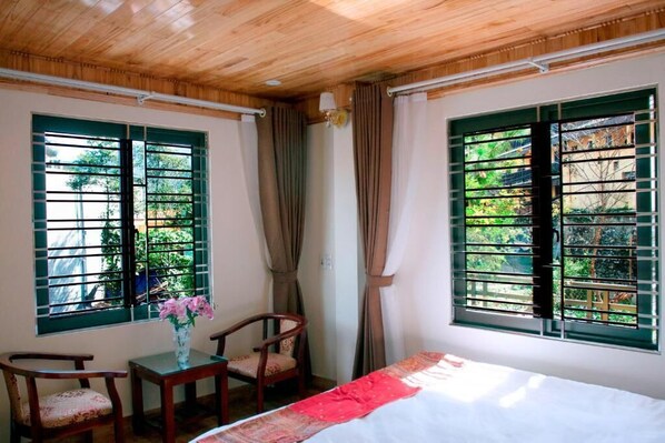 Una habitación con cama, una mesa con sillas y ventanas con cortinas.