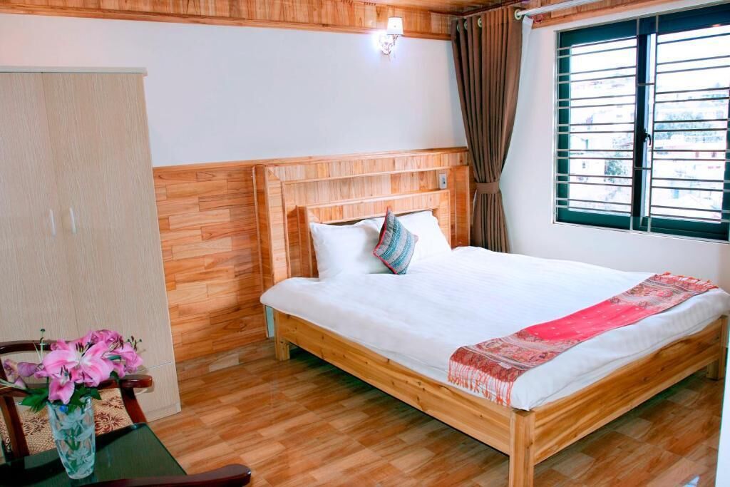 A wooden-framed bed with white bedding, a vase with flowers, and a window with curtains.