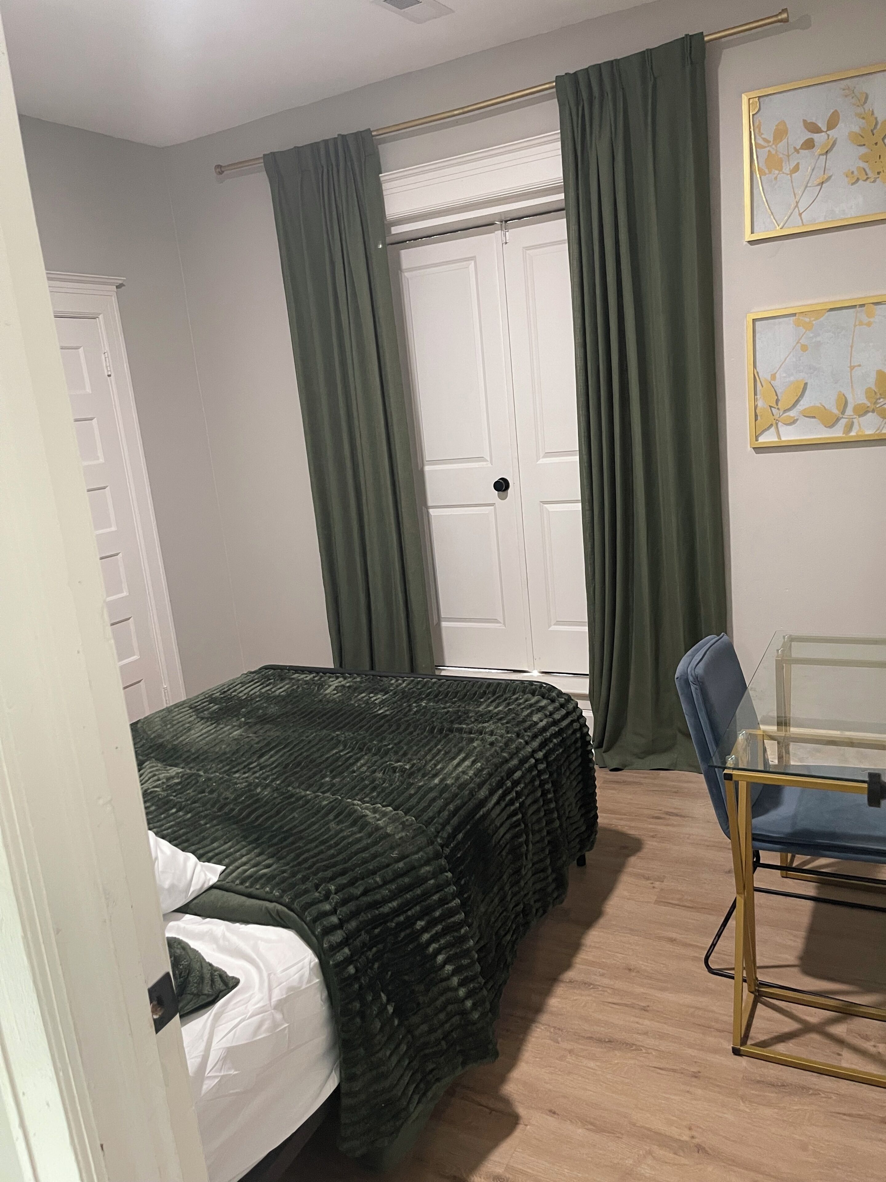 A bedroom with a bed, a chair, a door, and a window with curtains.