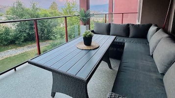 A balcony with a table and seating area, overlooking a scenic landscape.