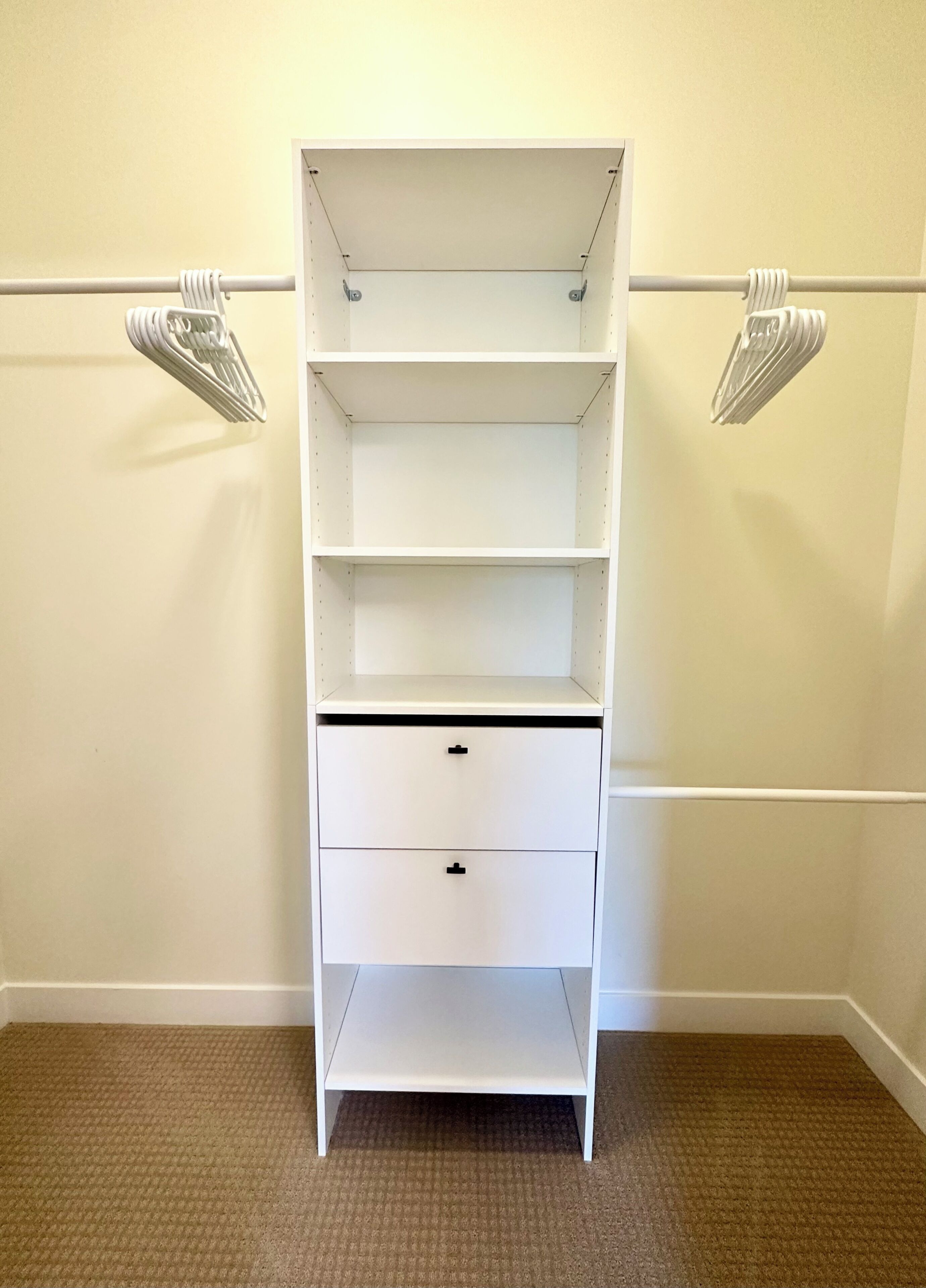 A white closet with three shelves and two drawers, against a beige wall with a carpeted floor.