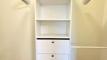 A white closet with three shelves and two drawers, against a beige wall with a carpeted floor.