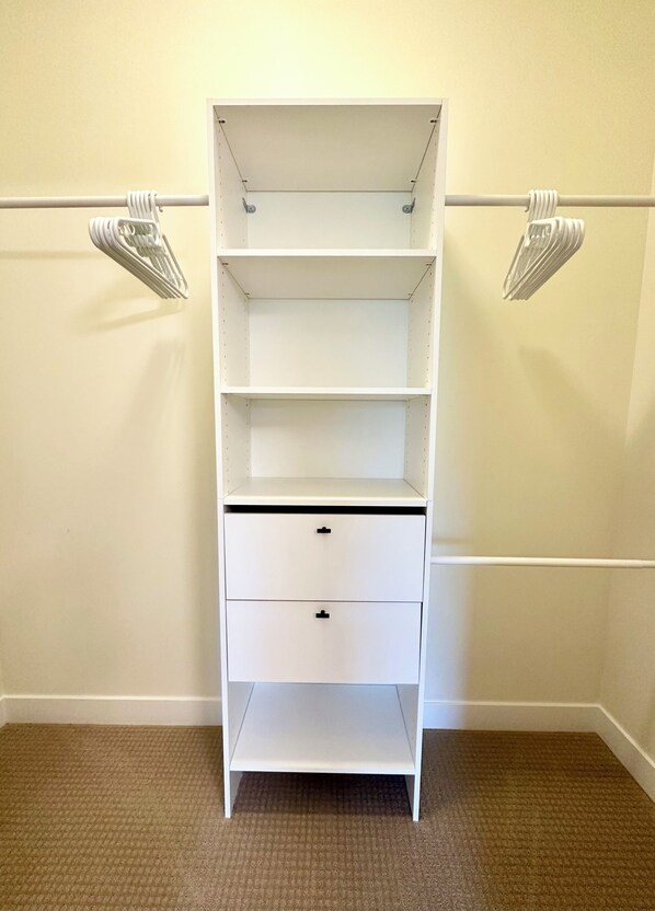 A white closet with three shelves and two drawers, against a beige wall with a carpeted floor.