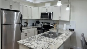 Una cocina moderna con gabinetes blancos, electrodomésticos de acero inoxidable, encimera de granito e iluminación colgante.