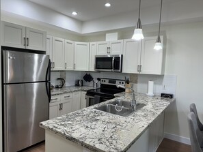 A modern kitchen with white cabinets, stainless steel appliances, a granite countertop, and pendant lighting.