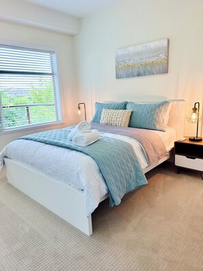 A bedroom with a bed, bedside tables, a window with blinds, and a wall-mounted artwork.