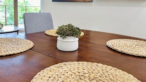 Una mesa de comedor con individuales tejidos, una planta en maceta, un aire acondicionado montado en la pared y un cuadro enmarco.