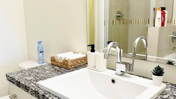 Ein Badezimmer mit weißem Waschbecken, einem Spiegel, einer Dusche und einer Toilette.