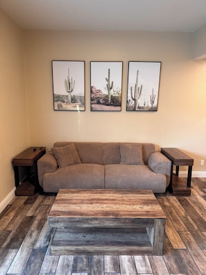 A living room with a brown sofa, wooden coffee table, and three framed desert landscape pictures on the wall. -     Modern Joshua Tree Retreat with Hot Tub, EV Charger, Views (Joshua Tree)