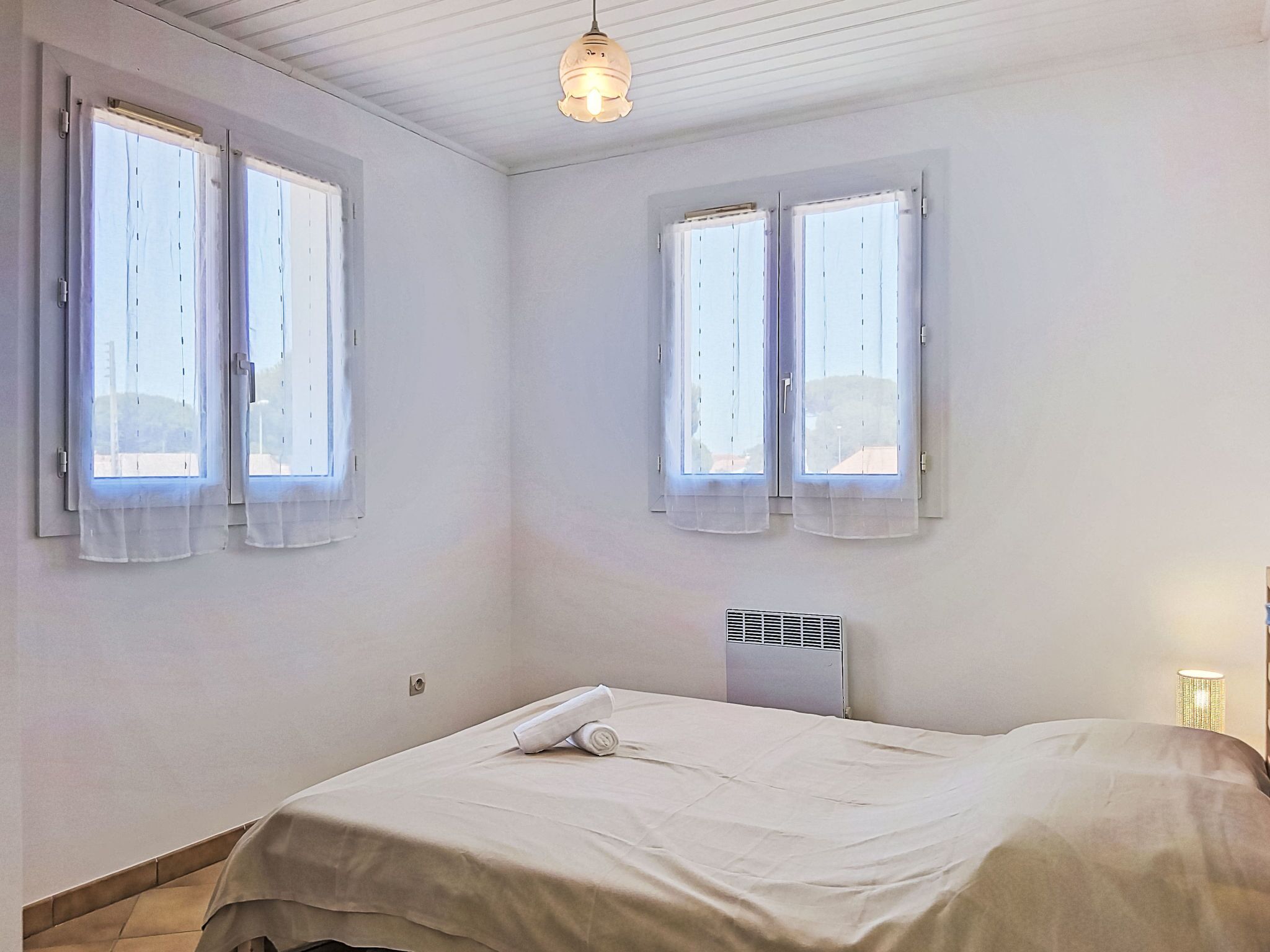 Ein Schlafzimmer mit zwei Fenstern, einem Bett, einer Wand-Klimaanlage und einer Deckenleuchte.