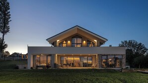 Ein modernes, zweistöckiges Haus mit großen Fenstern, einem Balkon und einem gepflegten Rasen.