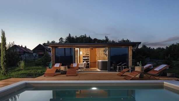 Ein modernes Haus mit Schwimmbad, Holzterrasse und Liegestühlen.
