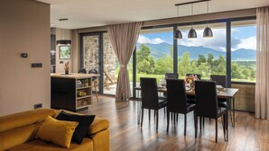 Ein modernes Wohnzimmer mit Essbereich, großen Fenstern und Blick auf die Berge sowie ein gemütliches, gelbes Sofa.