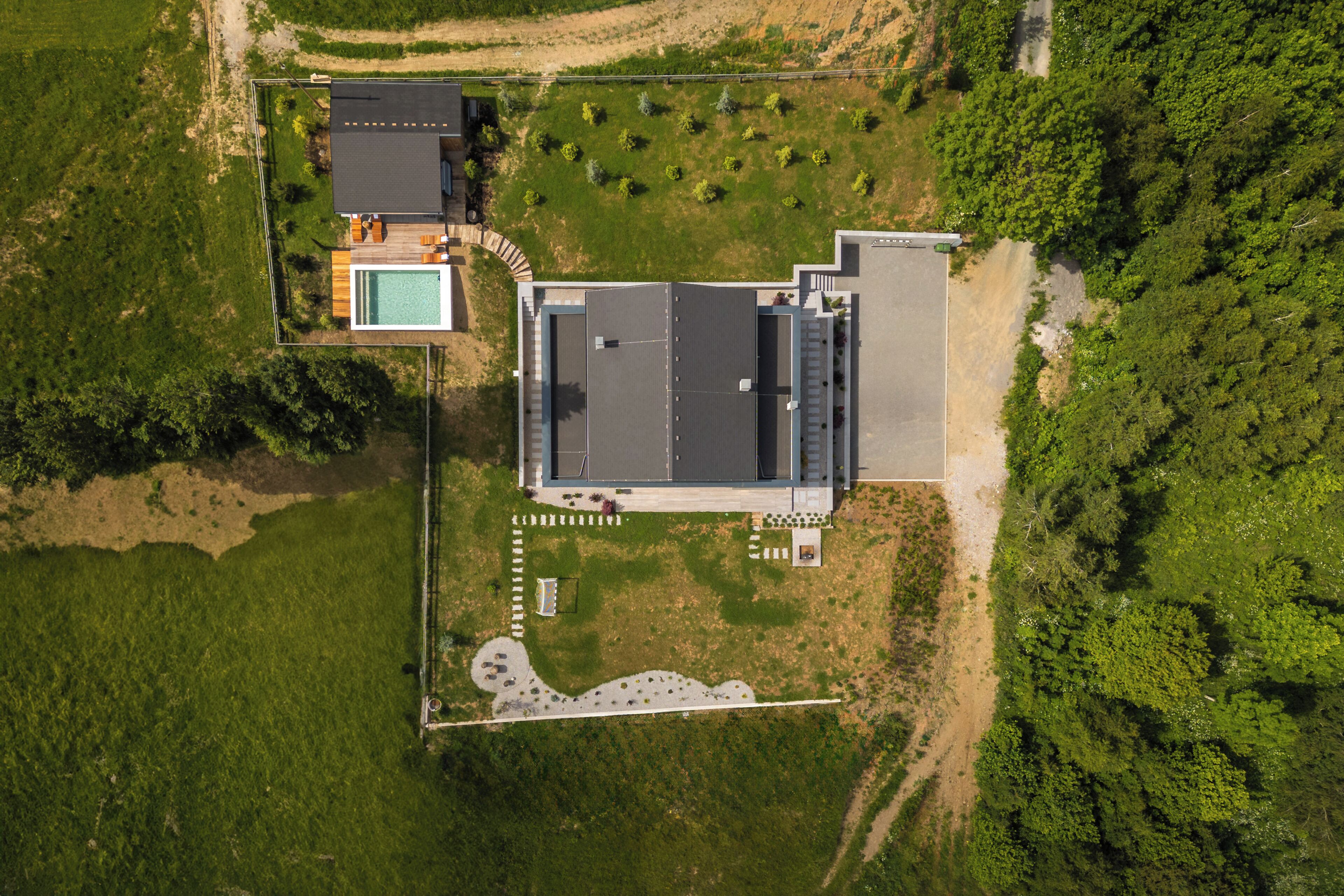 An aerial view of a modern building with a swimming pool, surrounded by greenery and a paved walkway.