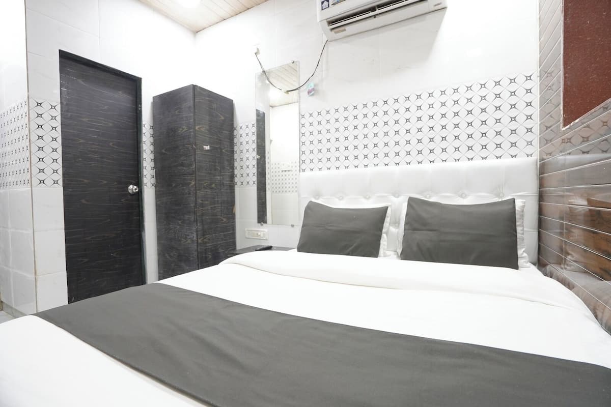A hotel room with a bed, a wardrobe, a mirror, and a wall-mounted air conditioning unit.