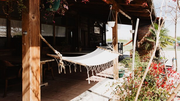 A wooden structure with a hammock, potted plants, and a brick wall.