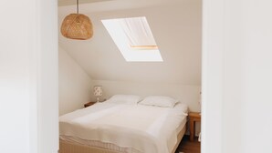 A bedroom with a bed, a bedside table, a lamp, a hanging light fixture, and a skylight.